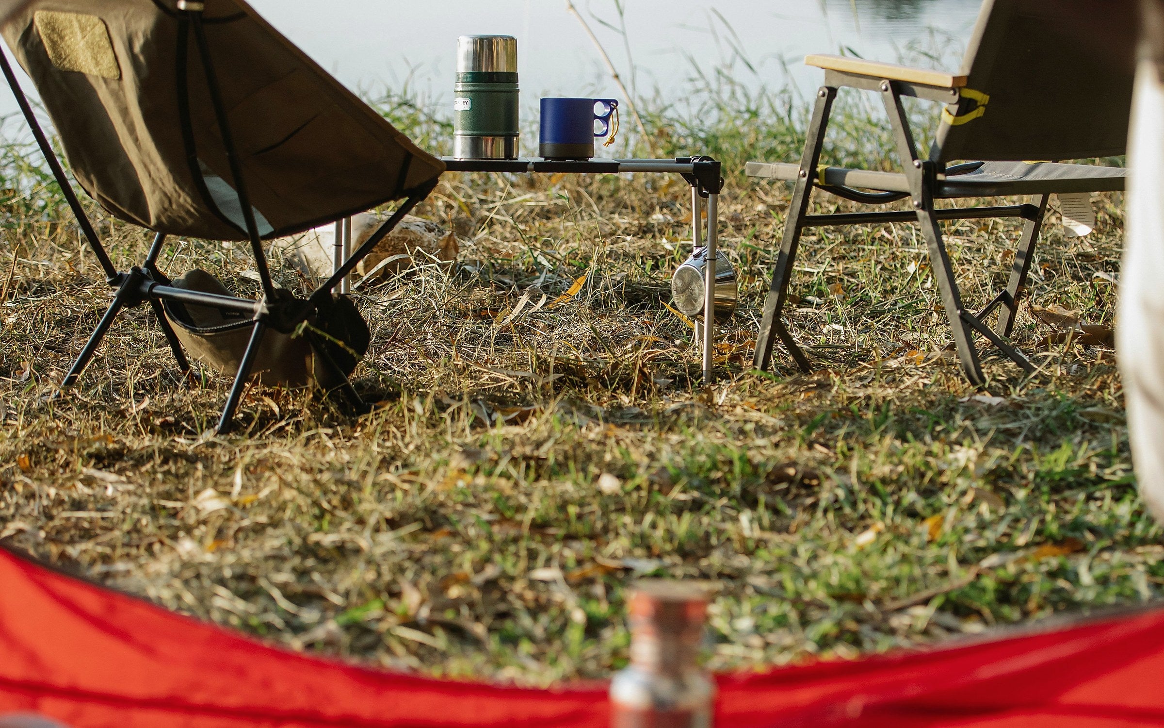 Portable chairs and a compact table viewed from a tent beside a lake